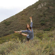 Dancer posing in middle of grassy area with a large hill in background
